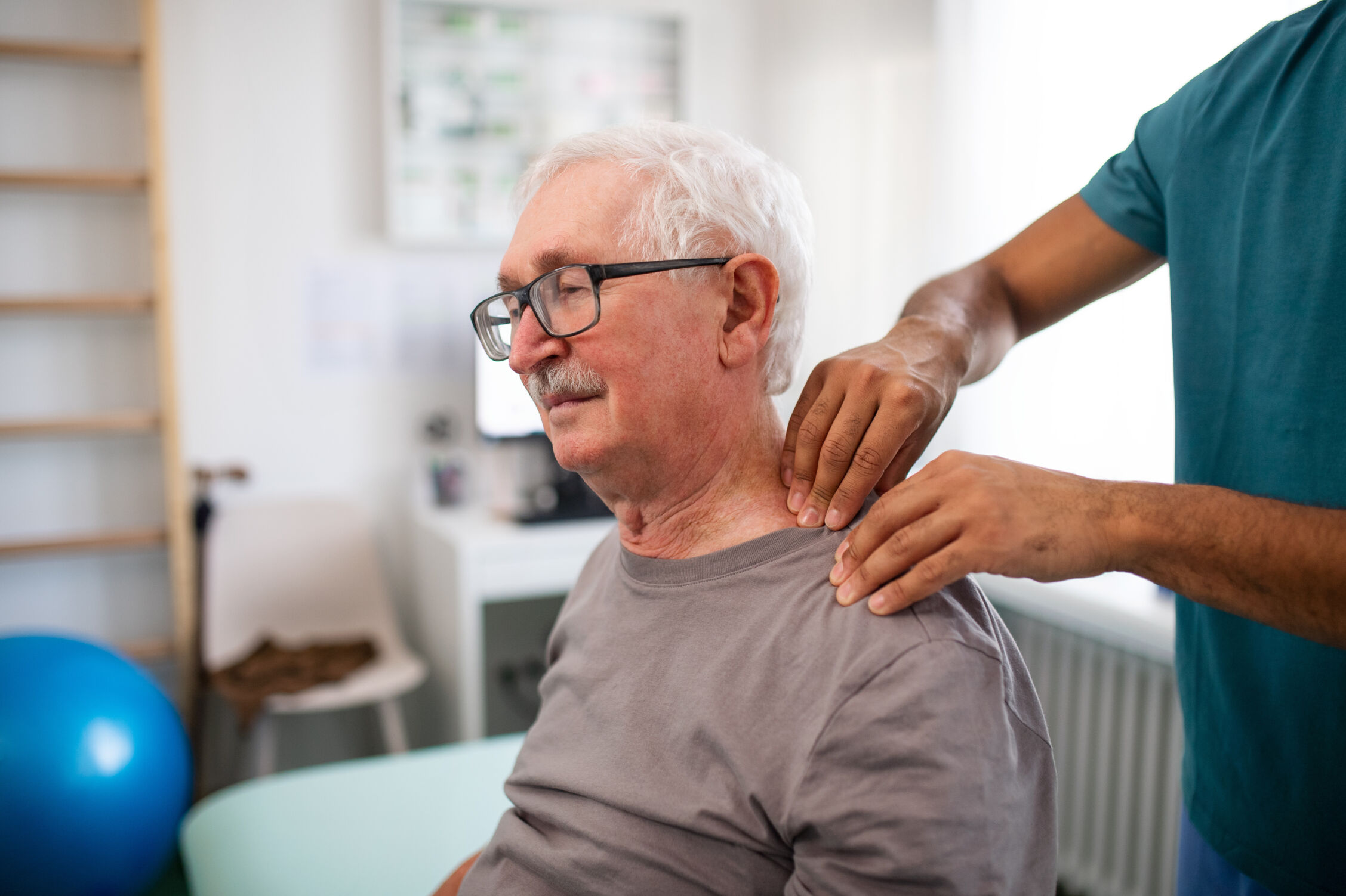Young physiotherapist massaging the neck of senior patient in a physic room